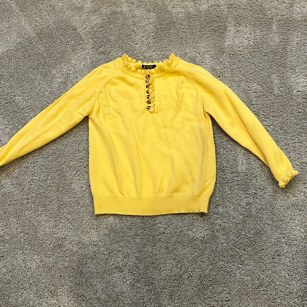 Woman’s sweater, ruffles on neck and sleeves, has buttons in the front